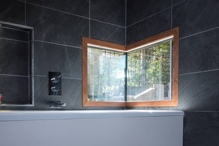 Unique corner window in dark tiled bathroom