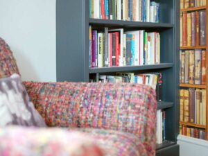 Dark blue bookcase with book wallpaper and multi coloured woollen chair